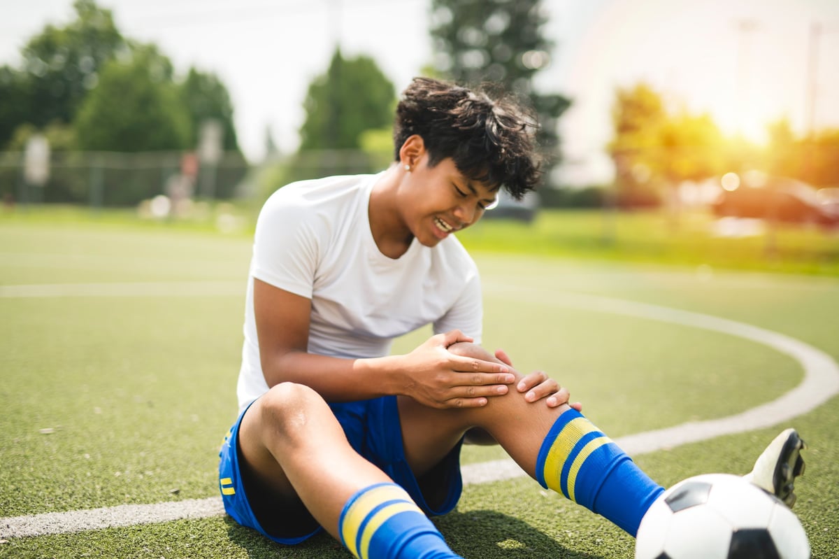 A nice Boy with soccer ball outside on field having injury